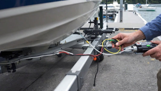 A boat trailer parked near the boat ramp, with the owner inspecting its wiring system.